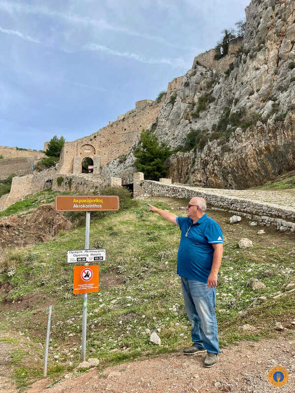 Akrocorinthos, the biggest ancient fortress of the Peloponnese. - Gastronomy Tours a man pointing at the sign towards Akroconthos